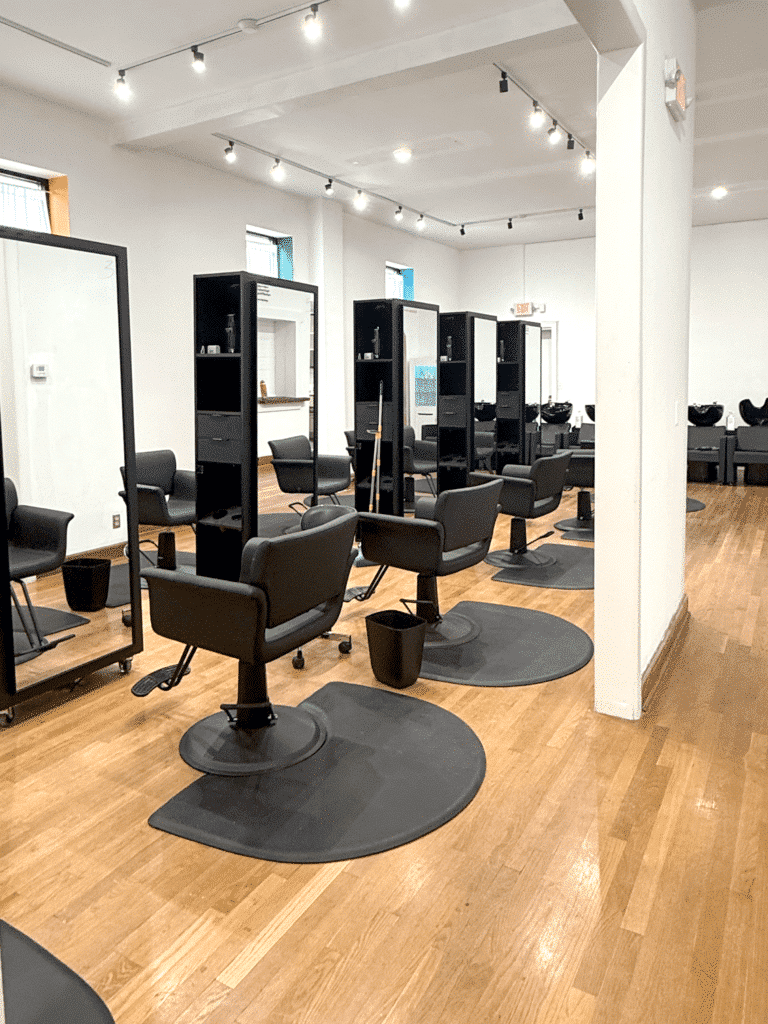 A modern hair salon interior with black styling chairs, mirrors, and wooden floors, arranged in a neat, well-lit space.